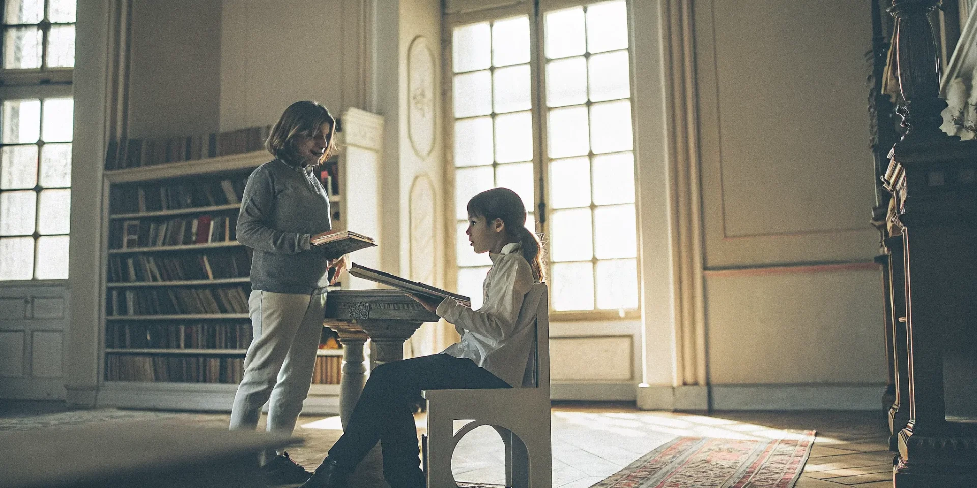 Professional governess tutoring a school-age child in an elegant UHNW home library